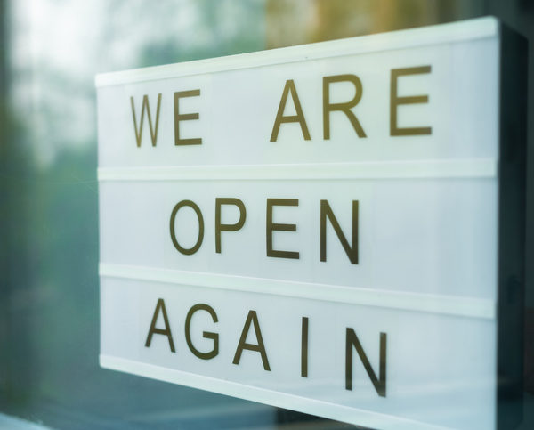 Lightbox with as sign we are open again behind a glass door of the cafe. We're open again after quarantine, video of small business owner. Please wear a face mask and keep your distance to protect