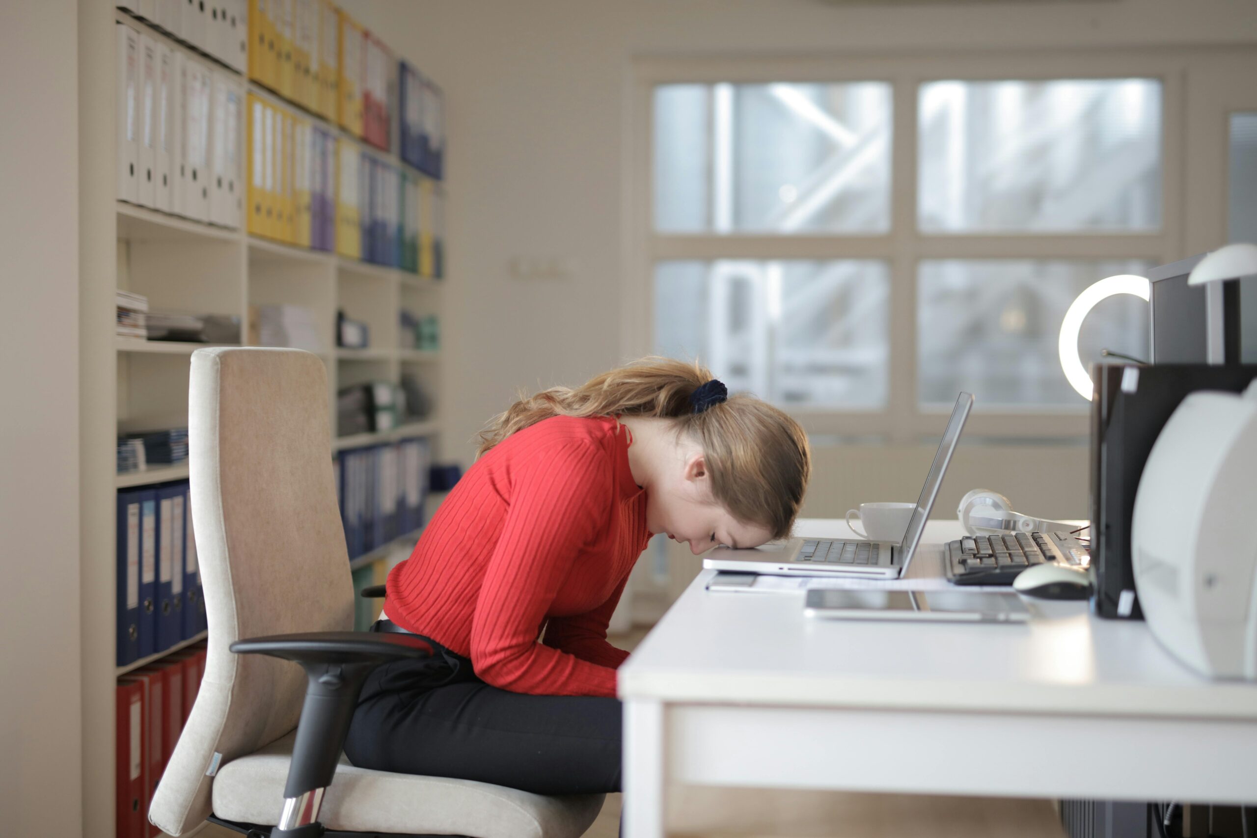 Woman asleep on a laptop at a desk, indicating overtime work fatigue