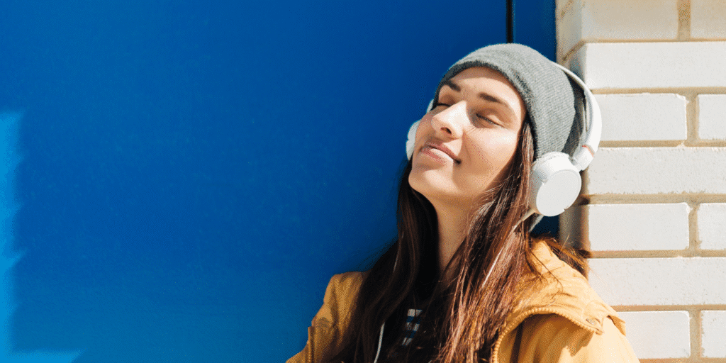 A young woman relaxes outdoors with headphones during her medical leave for mental health.