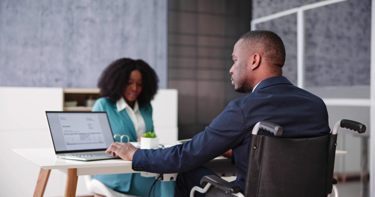 Professional workplace disability access with an employee in a wheelchair working on a laptop.