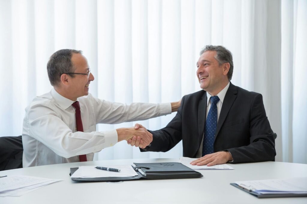 Two business professionals shaking hands after negotiating updated terms in employment contracts during mergers and acquisitions.
