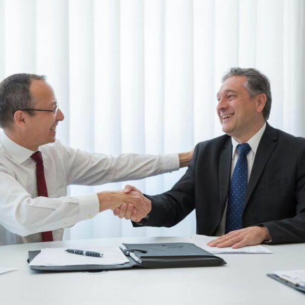 Two business professionals shaking hands after negotiating updated terms in employment contracts during mergers and acquisitions.