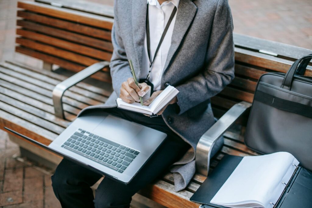 Professional employee taking notes while working on a laptop in a public space, reflecting remote work monitoring policies and compliance awareness.