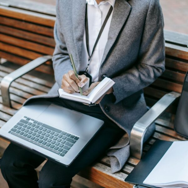 Professional employee taking notes while working on a laptop in a public space, reflecting remote work monitoring policies and compliance awareness.